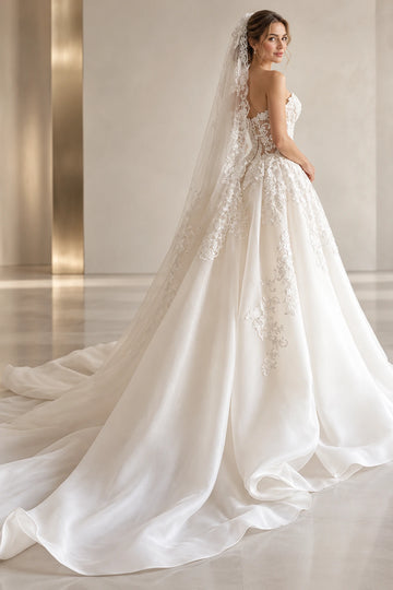 Rear three-quarter view of Vedress ball gown wedding dress showing a low lace back, full organza skirt and sweeping train beneath a veil.