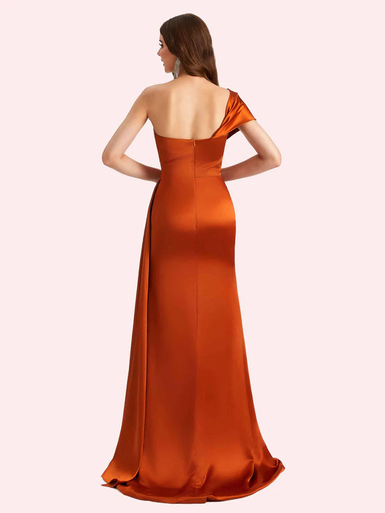 Open-back burnt orange satin formal gown with one-shoulder design, center zipper closure, side drape, and elegant floor-length skirt