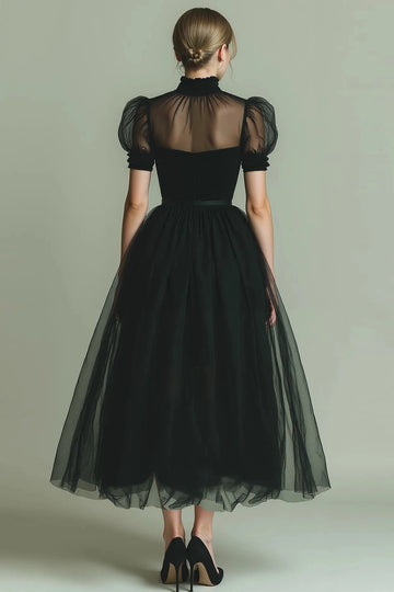 Back view of black tulle evening dress with a ruffled high collar, sheer upper back, puff sleeves, defined waist and layered A-line skirt.
