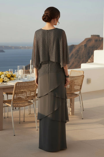 Charcoal gray formal mother of the bride gown featuring closed round back, sheer draped cape overlay, sparkling textured bodice and cascading layered skirt.