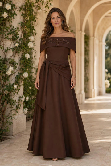 Chocolate brown A-line mother of the bride dress with an embellished off-shoulder neckline, fitted bodice, asymmetric draped waist and floor-length skirt.