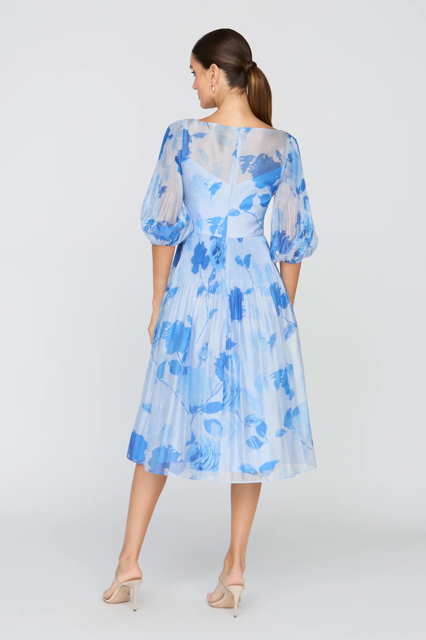 Back view of light blue floral midi dress with puff sleeves, back zipper closure, A-line skirt, and elegant floral chiffon-style overlay