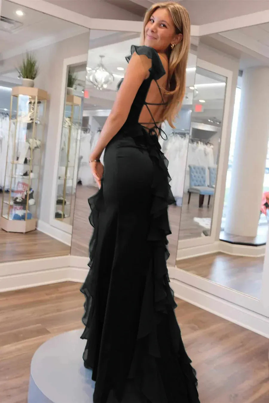 Back view of black satin formal dress with open lace-up back, ruffle strap detail, fitted silhouette, and ruffle slit skirt by VEDRESS