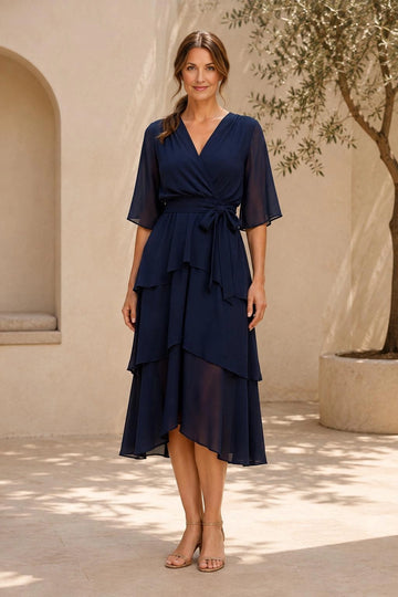 Navy blue A-line mother of the bride midi dress featuring surplice V-neckline, sheer flutter sleeves, tied waist and asymmetrical tiered skirt, front view.