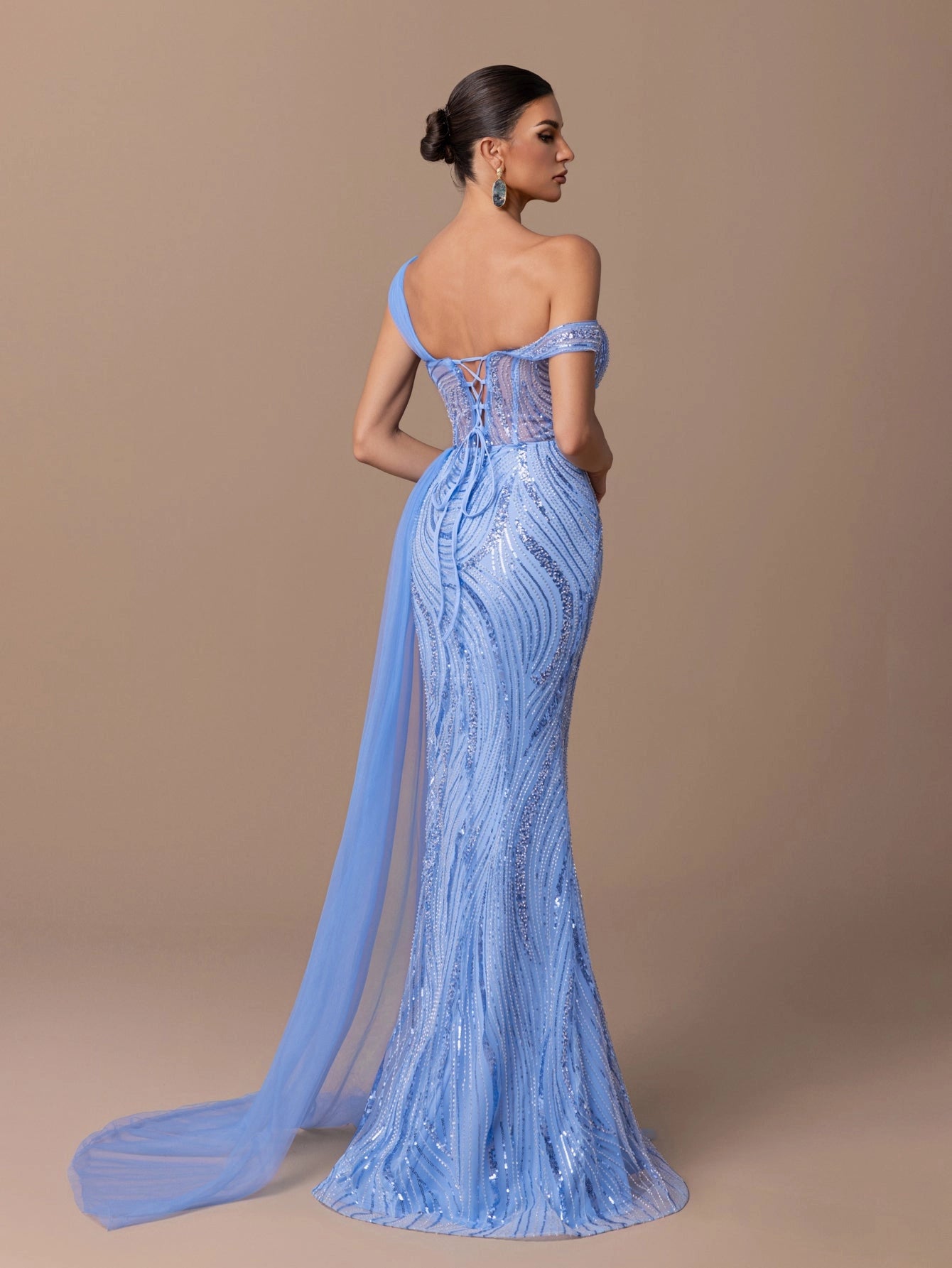 Back view of blue sequin tulle mermaid prom dress featuring asymmetric shoulder straps, lace up corset back, sparkling embellishments and sheer side drape