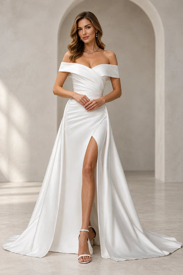 Vedress off-shoulder wedding dress with a folded neckline, draped waist, high leg slit and flowing overskirt.