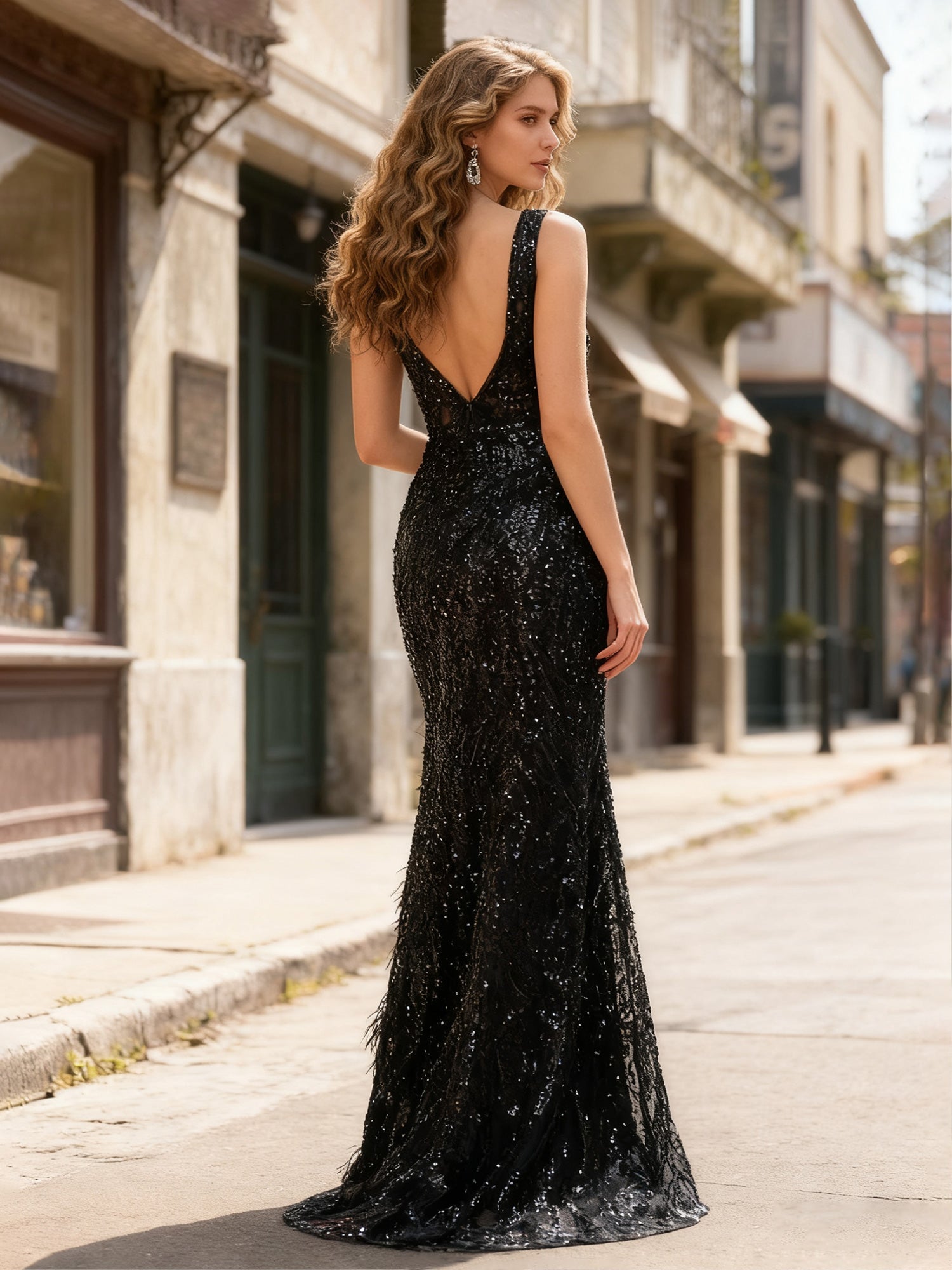 Back view of sleeveless sequin formal gown with deep V open back, fitted mermaid shape, feather detail, and floor-length train by VEDRESS