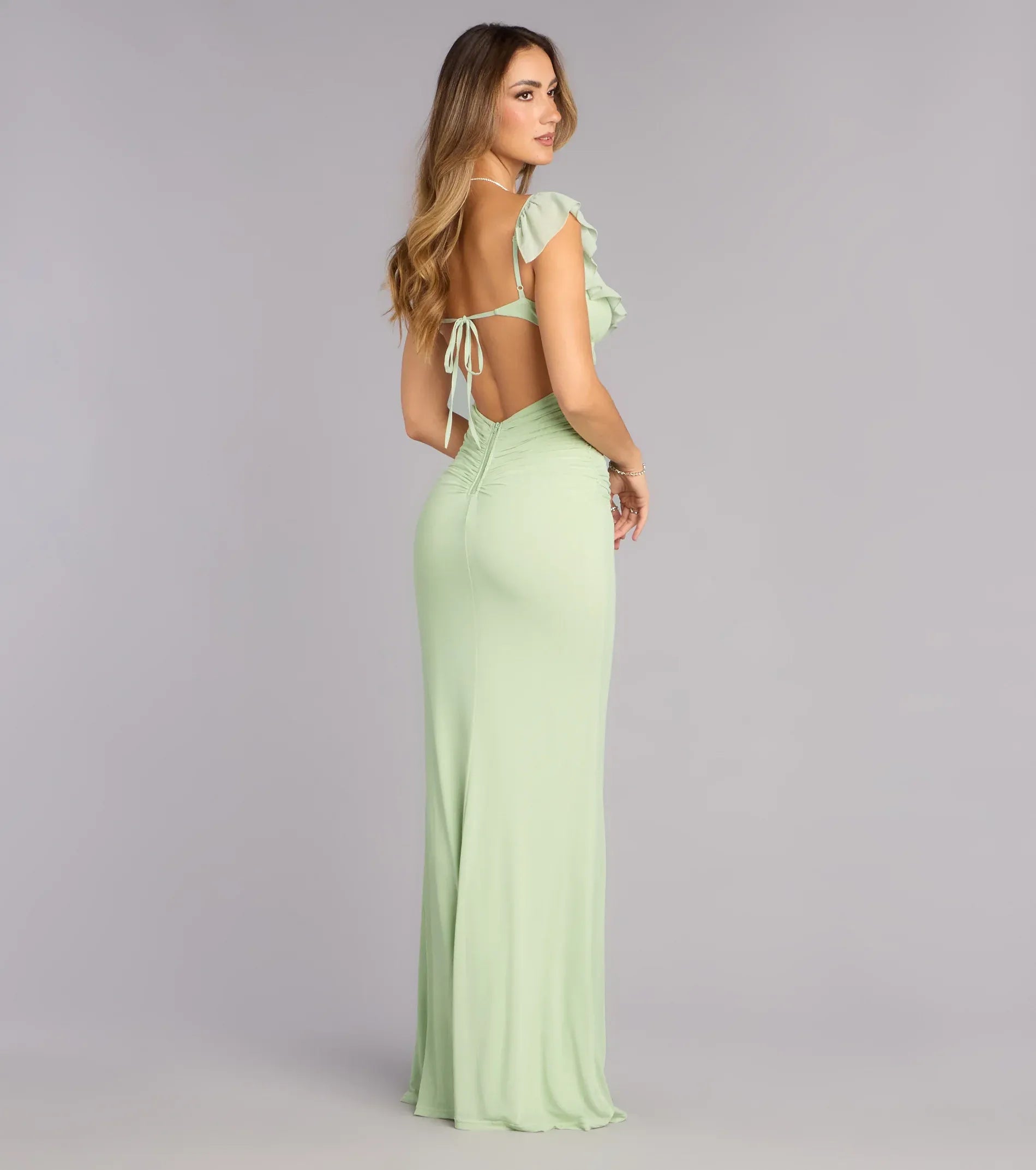 Back view of open back ruffle formal dress with tie detail, zipper closure, and fitted floor-length skirt