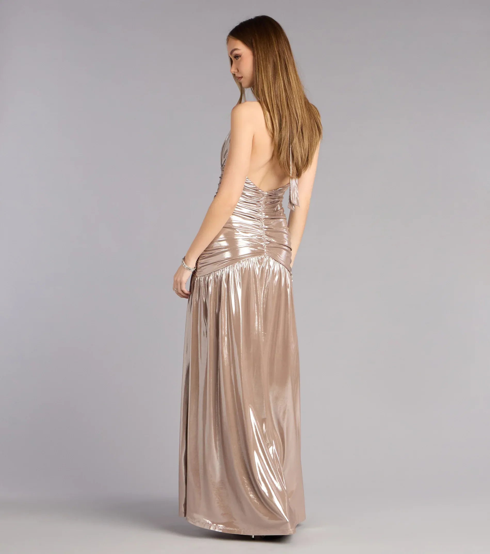 Back view of champagne metallic halter formal dress with low open back, ruched bodice, and flowing A-line skirt