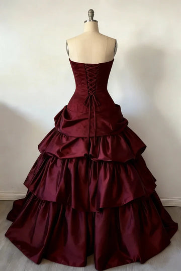 Back view of burgundy satin ruffled ball gown with lace-up corset closure, strapless bodice, and dramatic tiered skirt
