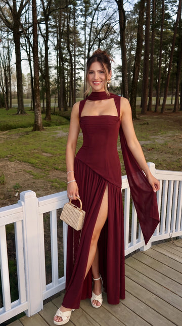 Burgundy A-line prom dress with square neckline, fitted asymmetrical bodice, flowing scarf detail, thigh-high slit, and floor-length gathered skirt by Vedress.