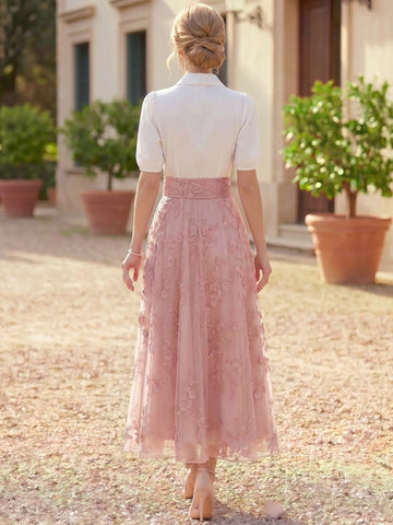 Back view of Vedress ankle-length wedding guest dress with a fully covered white bodice, wide pink lace waistband and floral embroidered skirt