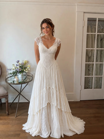 Vedress lace A-line wedding dress with a scalloped V neckline, cap sleeves, pointed waist and tiered floor-length skirt with a train, front view