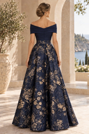 Back view of navy blue mother of the bride gown with V-shaped off-shoulder back, center zipper, defined waist and gold floral A-line skirt