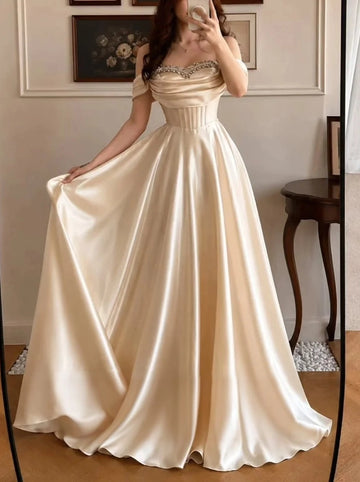 Front view of a champagne satin Vedress A-line prom dress with a beaded sweetheart neckline, off-shoulder sleeves and corset-style bodice.