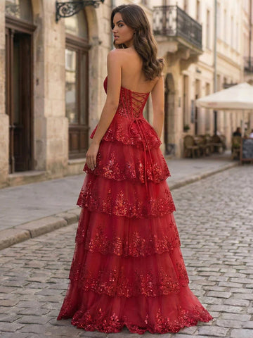 Vedress red tiered ruffle prom dress with a low lace-up corset back, trailing waist ties, and sparkling floral details, back view.