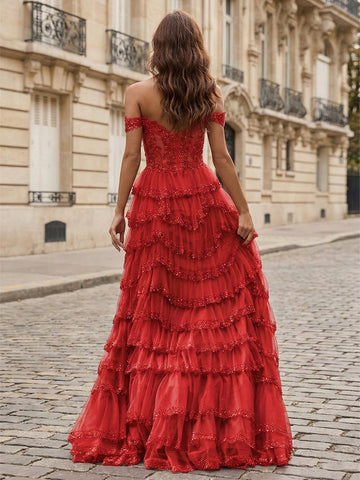 Back view of a red tiered tulle prom dress with a sheer illusion bodice, floral appliqués and beaded ruffle edges.